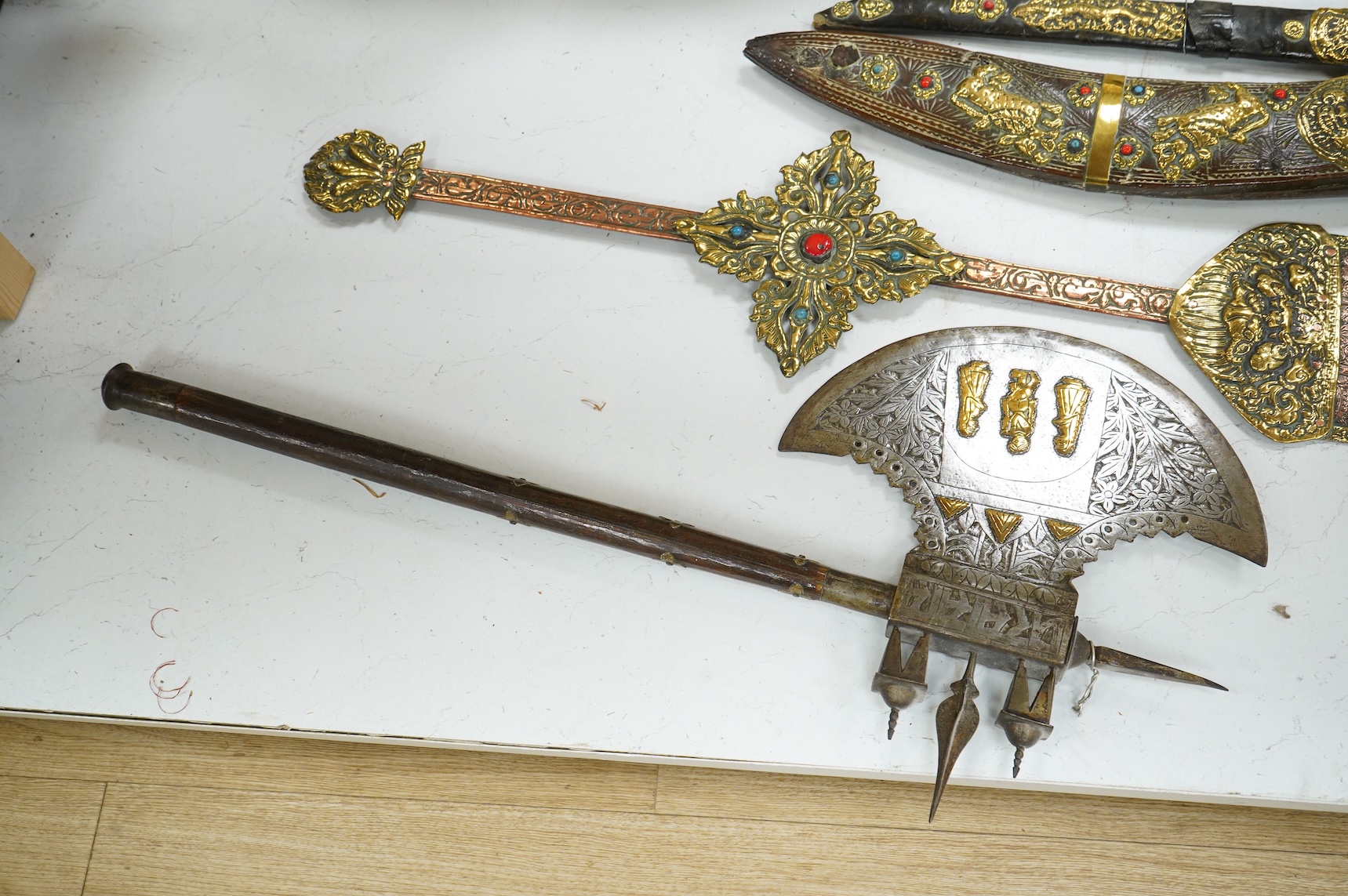 A decorative Indian axe, the large head inlaid with brass Hindu figures, together with a brass mounted North Indian kukri, another similar knife with bone handle, and a large shovel-shaped copper and brass item possibly